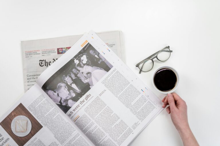 Overhead view of newspaper reading with coffee and glasses on a white table.